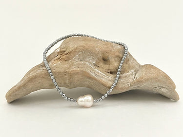 Armband Lucy aus Hämatitperlen mit silbrigem Glitzern und einer Barockperle auf einem Holzstück dekoriert