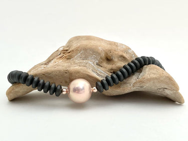 Halskette aus dunkelgrauen Steinscheiben mit einer hochwertigen großen Süßwasserperle in zartem Rosé vorne in der Mitte eingefügt